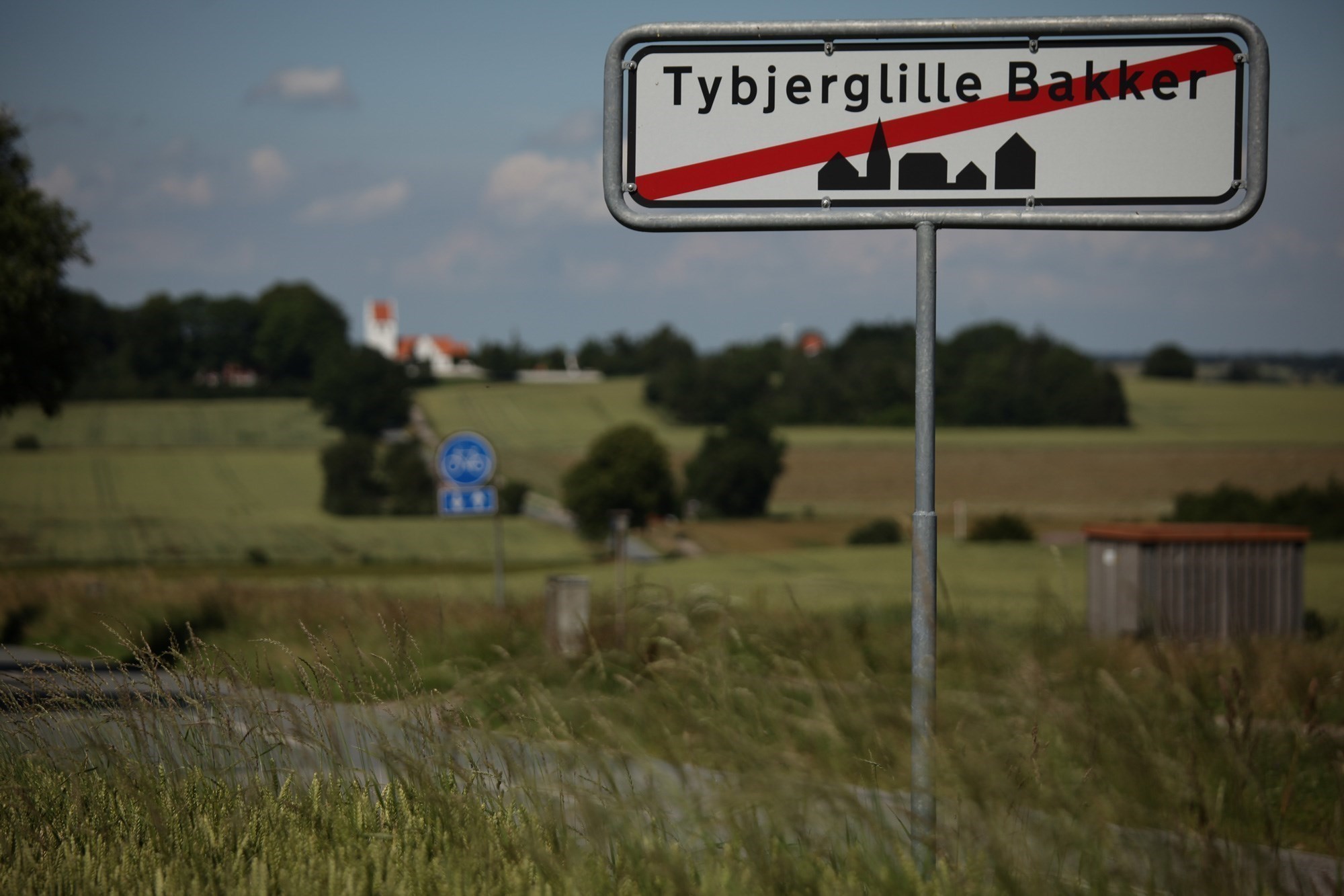 Byskilt på vej ud ad Tybjerg med gule marker i baggrunden