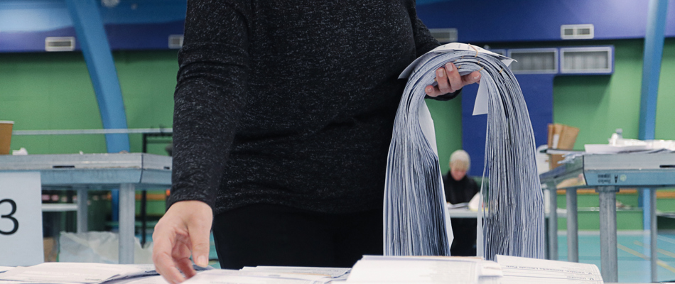 Foto viser en kvindes arm, der holder en stor bunke stemmesedler. Billedet er taget på valgaftenen under optælling ved kommunalvalget i 2021.