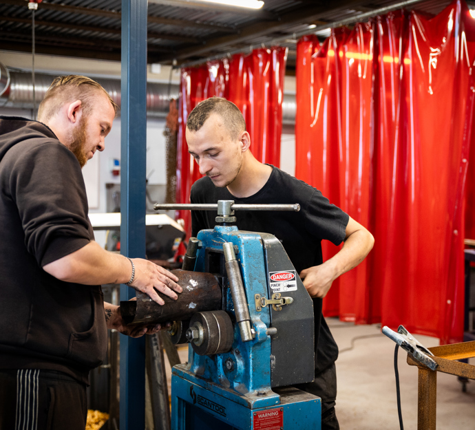 To drenge arbejder med et stykke metal ved en maskine