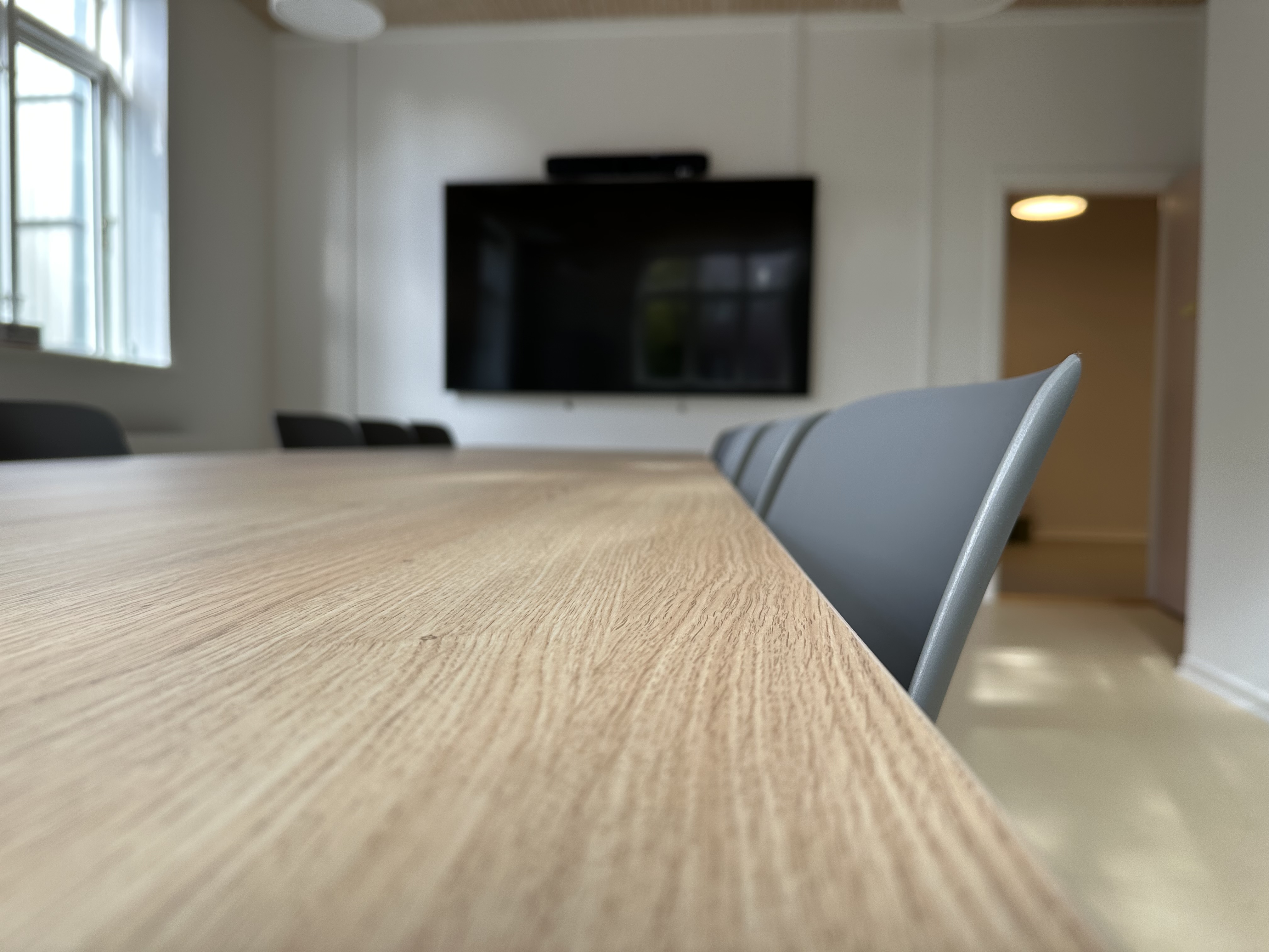 Mødelokale med bord med stole rundt om og tv-skærm på væggen.