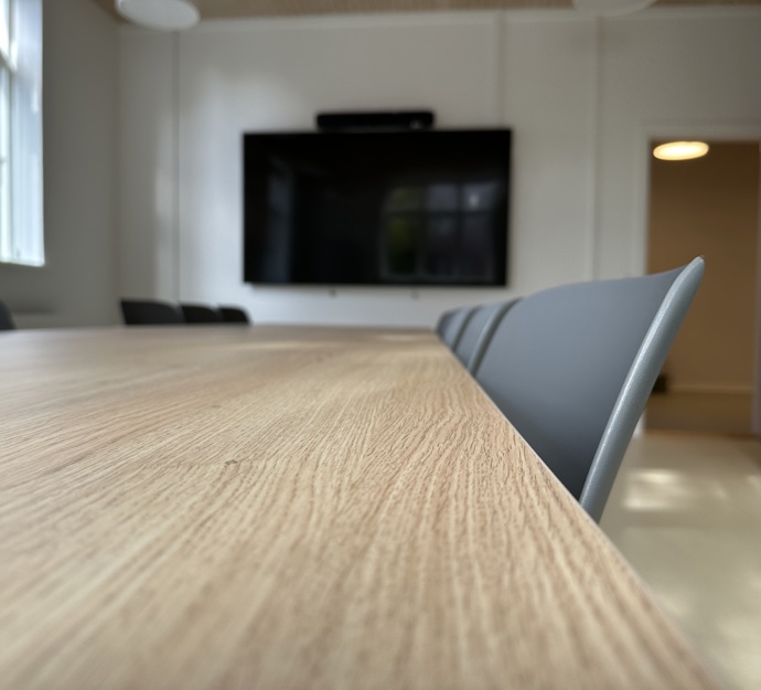 Mødelokale med bord med stole rundt om og tv-skærm på væggen.