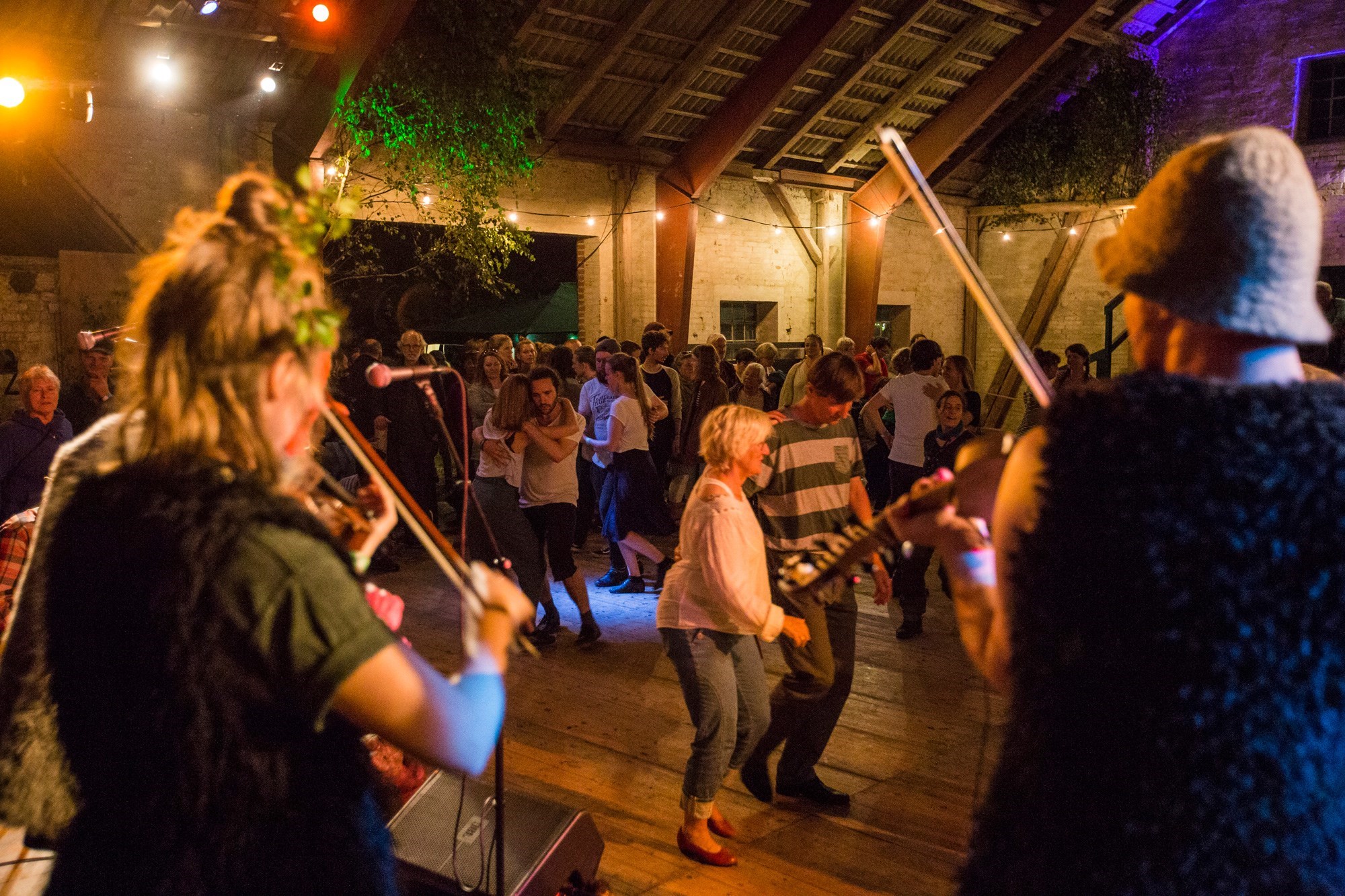 Musikanter spiller violin imens mennesker danser sammen foran dem