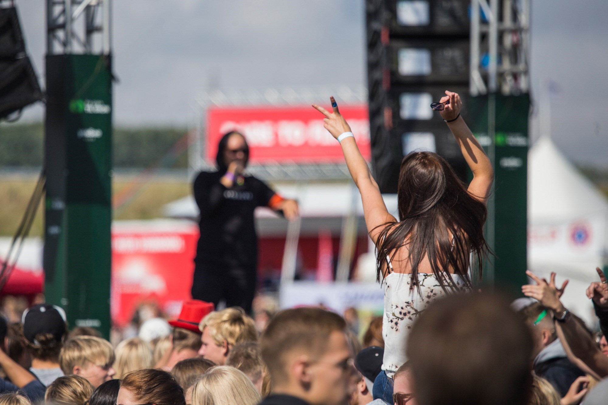 En kvinde blandt publikum sidder på skuldrene og gestikulerer mod en mandlig rapper på scenen