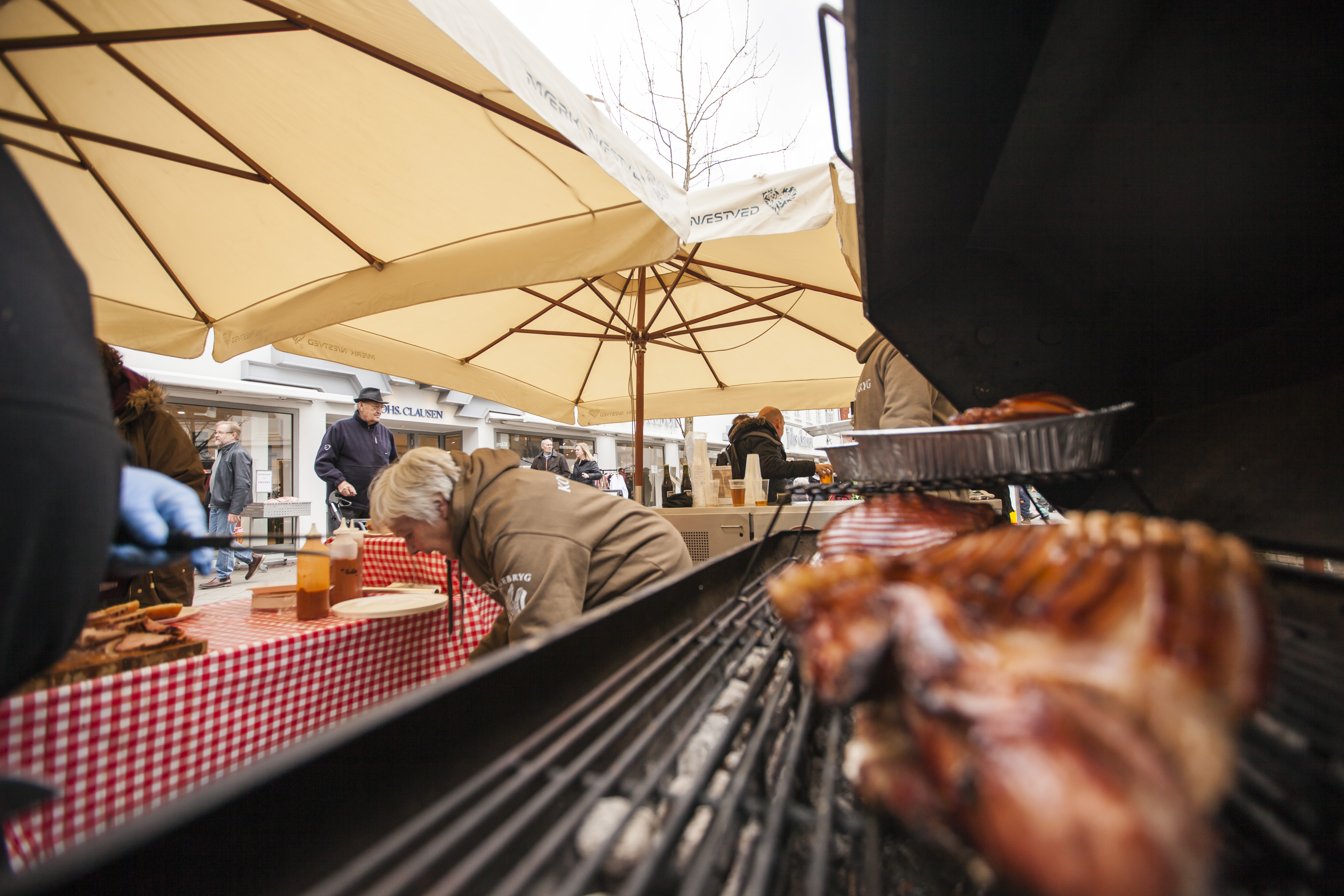 Kød på grill, parasoller og personer i baggrunden. 