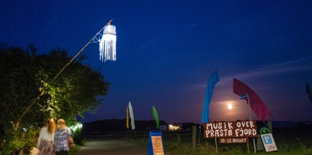 To piger på vej ned ad en sti hvor et skilt annoncerer Musik Over Præstø Fjord