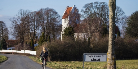 En pige er cyklet forbi byskiltet på vej ind til Toksværd med kirken på hendes højre side