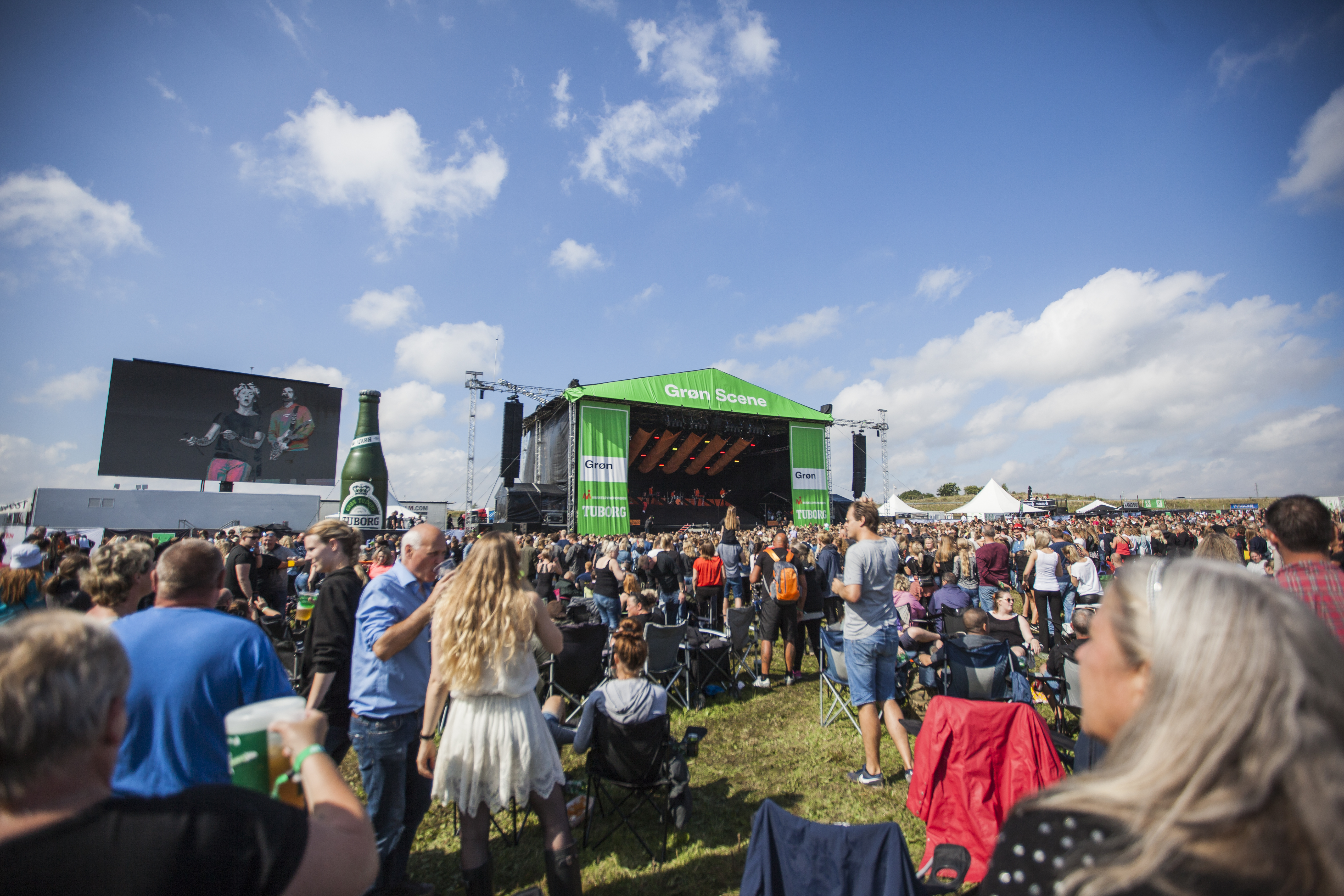Publikum udendørs, der står og kigger op med en grøn scene til Grøn Koncert. 