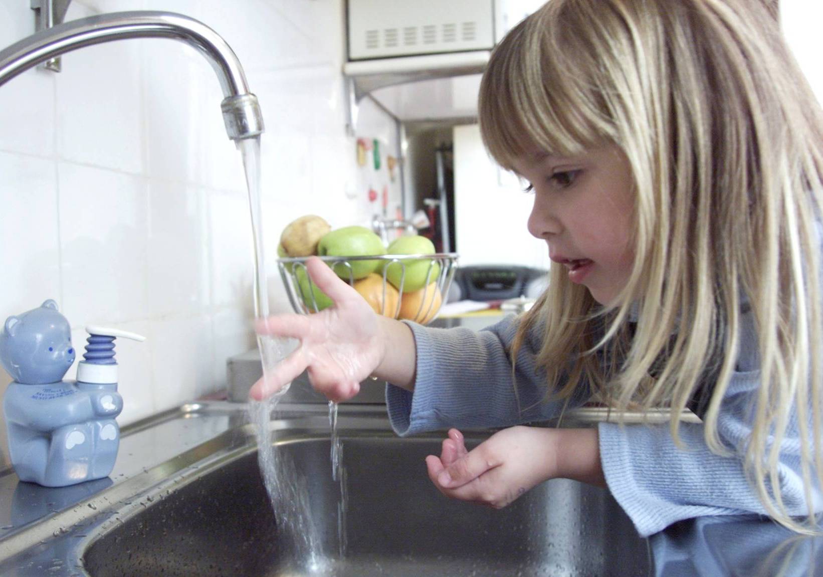 Pige holder en finger under strålen fra vandhanen i køkkenet
