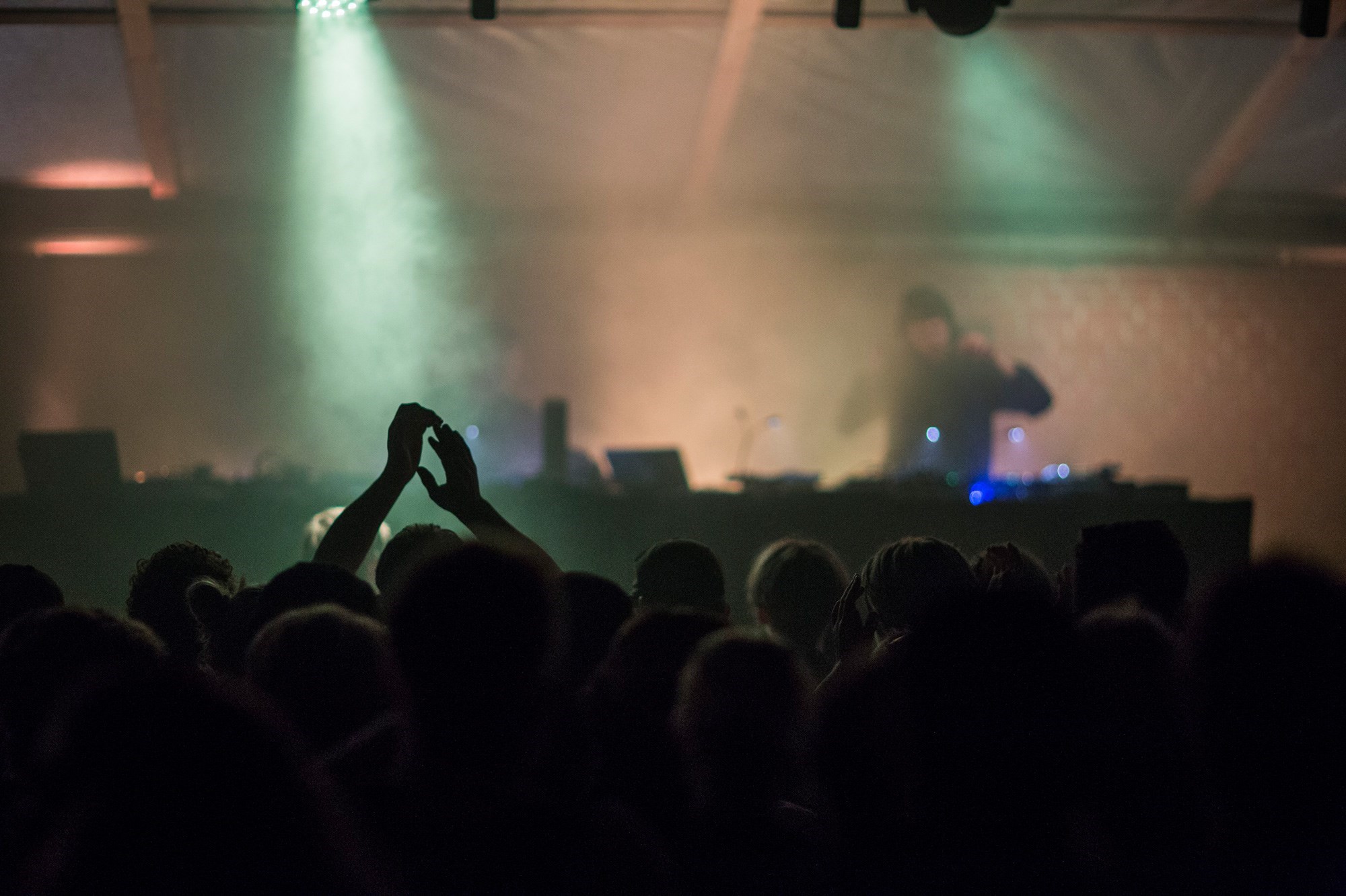 Hænder klapper foran en scene er oplyst med røg og lys foran i Næverland Næstved