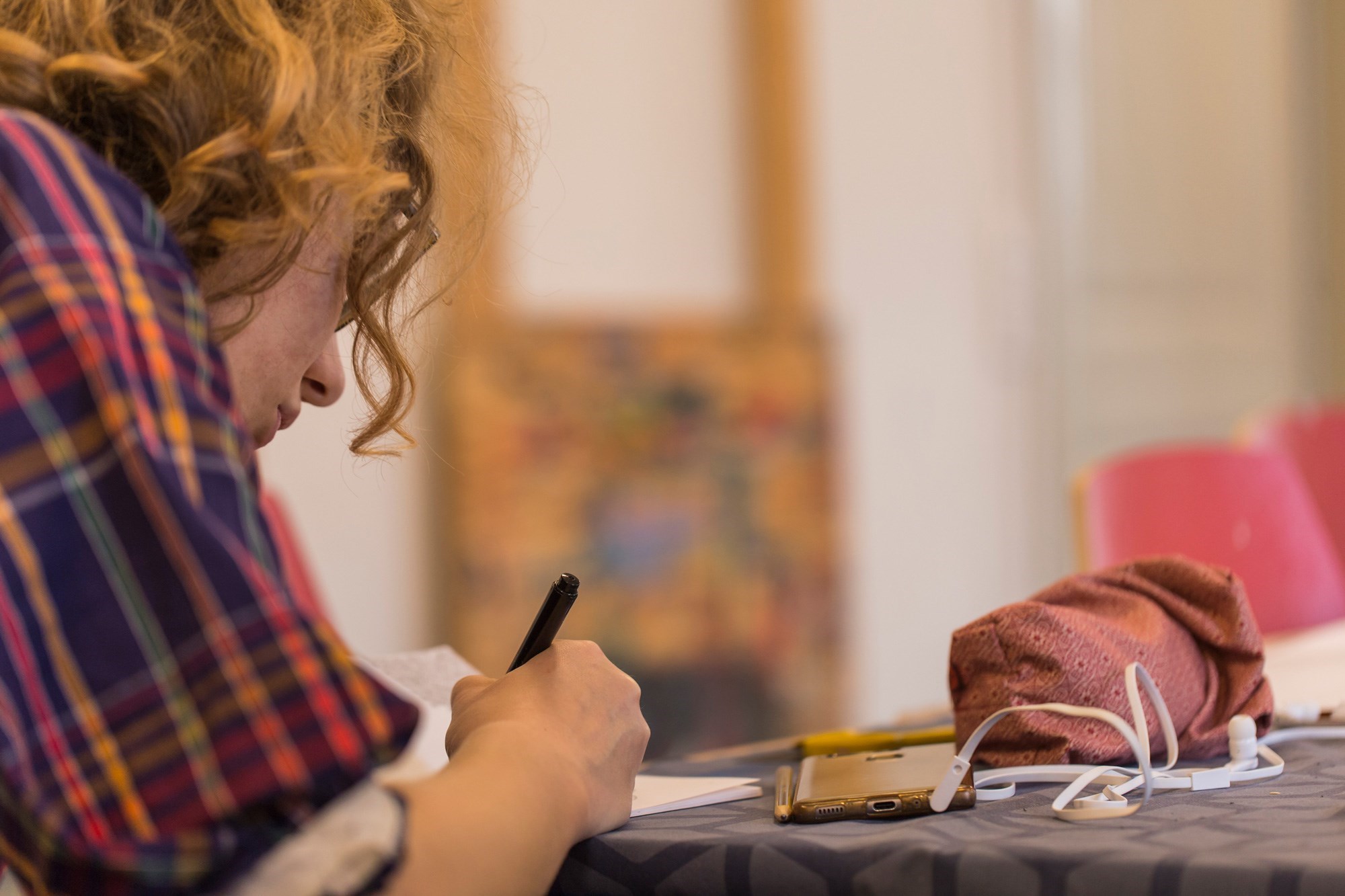 En pige er ved at skrive på et papir. På bordet ligger et øretelefoner og et penalhus