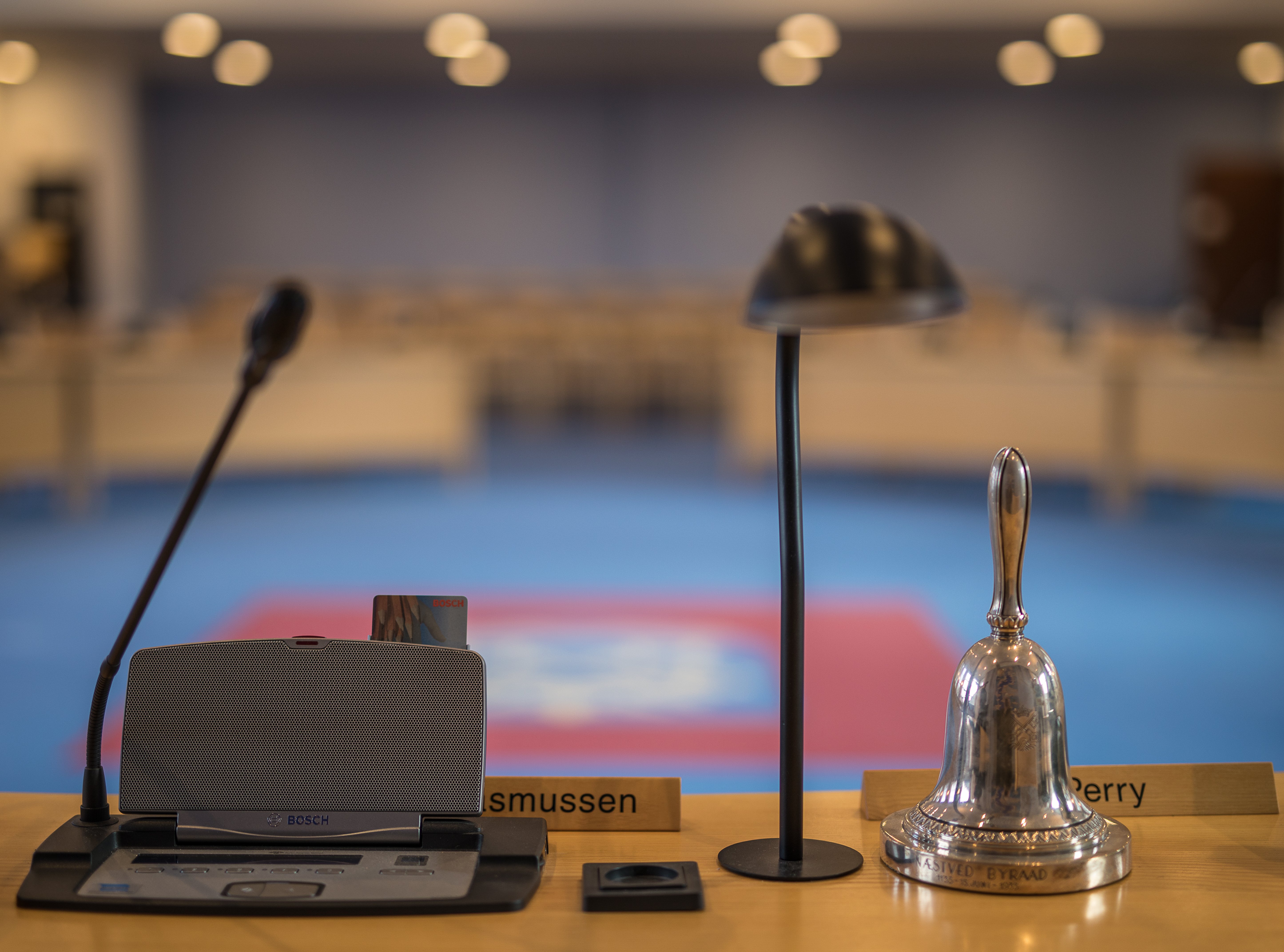 Byrådssalen med bord, mikrofon, lampe og klokke - formandens plads