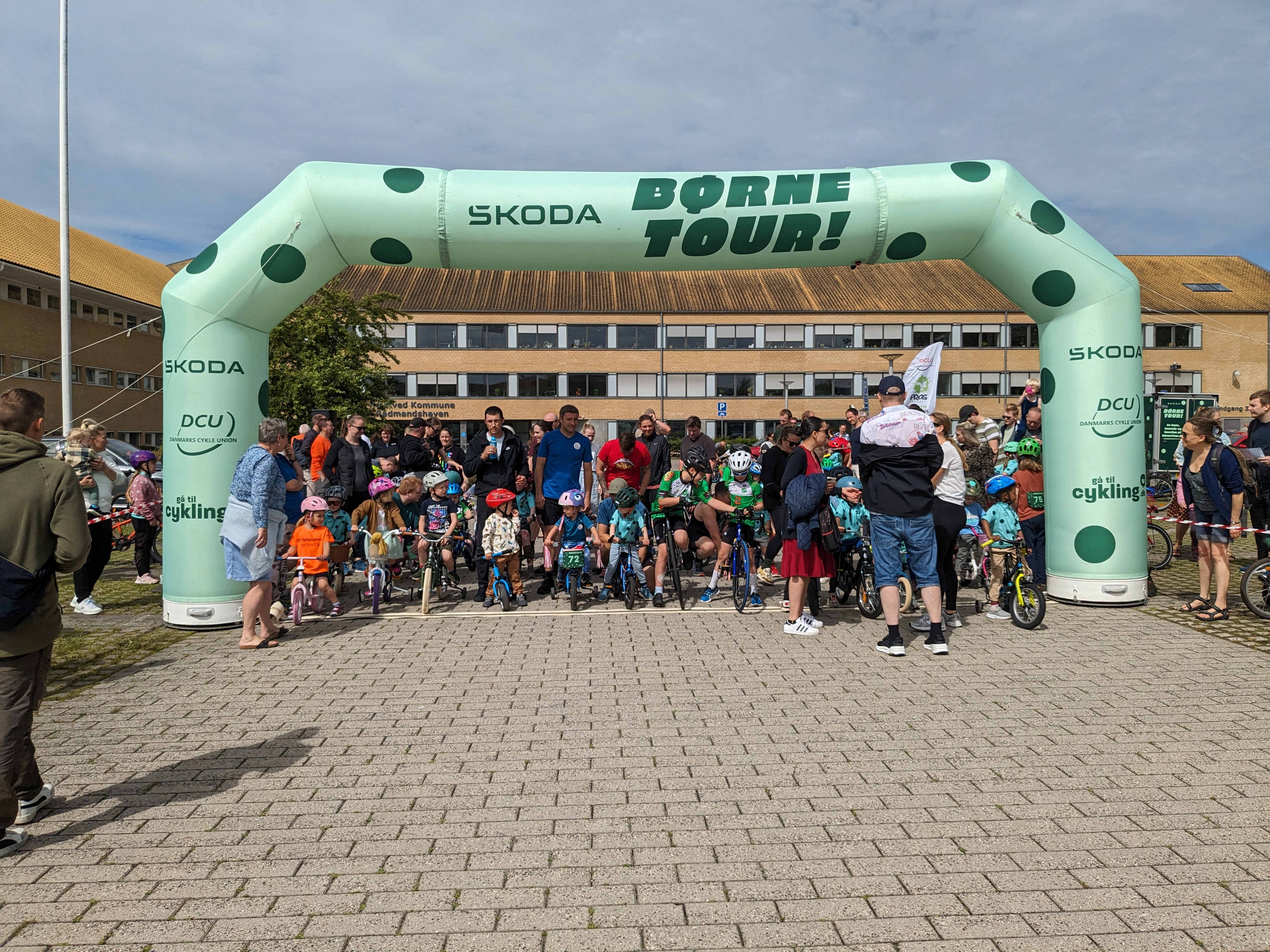 Børn med cykler står klar under oppustelig startportal. 