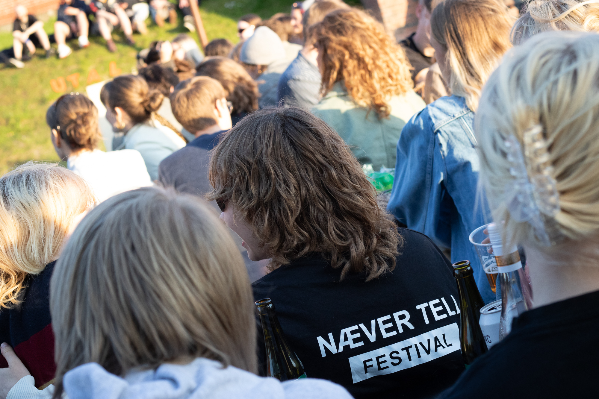 Publikum udendørs, der er en med en trøje, hvor der står Næver Tell Festival. 