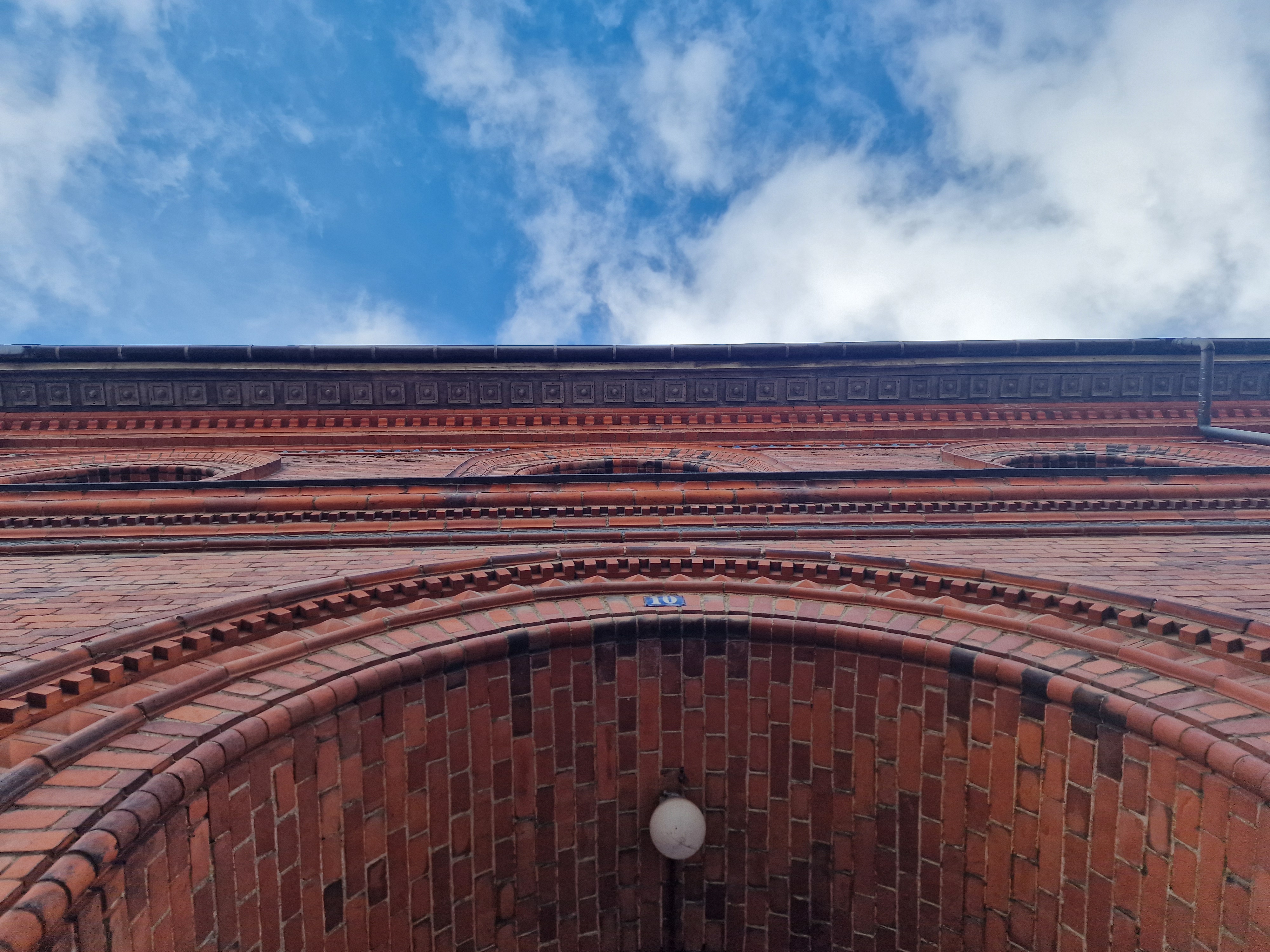 Indgangsdør til gammel murstenbygning nederst og blå himmel med små skyer øverst. 